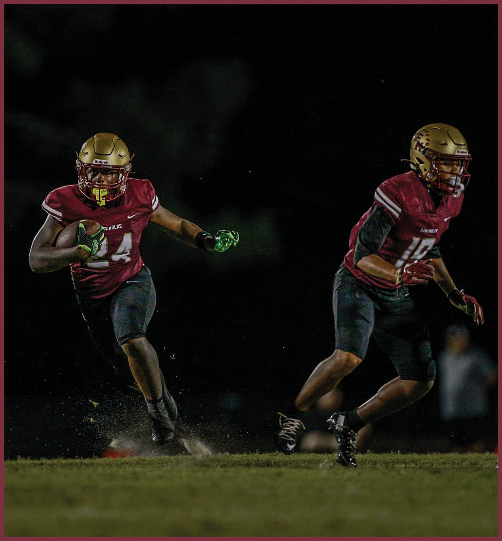 A person wearing a glove raises an arm while two people in football helmets and uniforms look ahead during a nighttime outdoor event. Description generated by AI