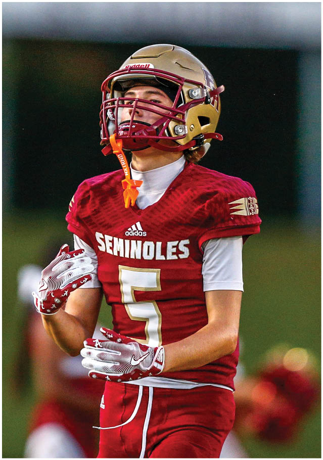 A person wearing a football helmet and a white jersey with the word “Seminoles" and the number 2 is running on a field with another player in red blurred in the background. Description generated by AI