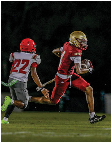 People wearing football helmets and uniforms are running on a field during a game or practice. Description generated by AI