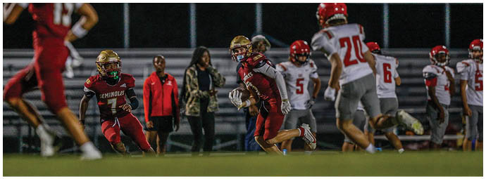 People wearing red and white football uniforms are actively engaged in a play on a football field. Description generated by AI