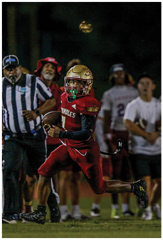 A person wearing a football helmet and uniform is running while holding a football, preparing to throw it. Description generated by AI