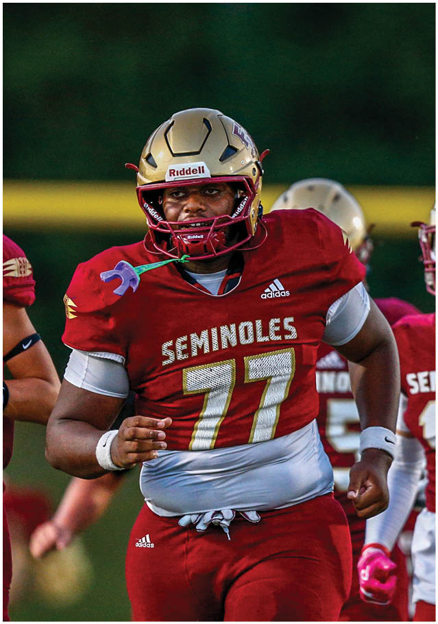 A person wearing a football uniform with a gold helmet and red pants is in mid-kick on a football field. Description generated by AI