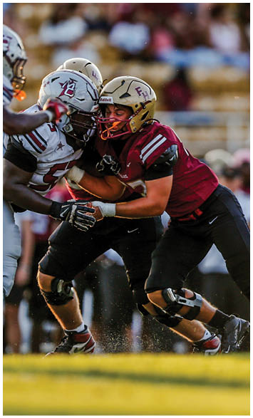 Two people wearing gold football helmets and white jerseys with “Seminoles" written on them are engaged in a conversation or huddle under bright lights. Description generated by AI