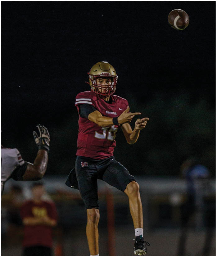 A person in a dark uniform is running with a football while being tackled by a person in a white and gold uniform during a football game. Description generated by AI