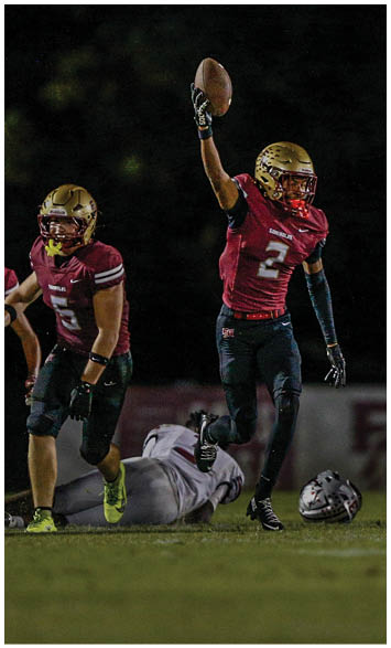 Two people wearing gold football helmets and white jerseys with “Seminoles" written on them are engaged in a conversation or huddle under bright lights. Description generated by AI