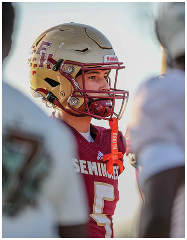 A person wearing a maroon football jersey with the word Seminoles and a helmet is standing outdoors with a red mouthguard attached to the helmet. Description generated by AI