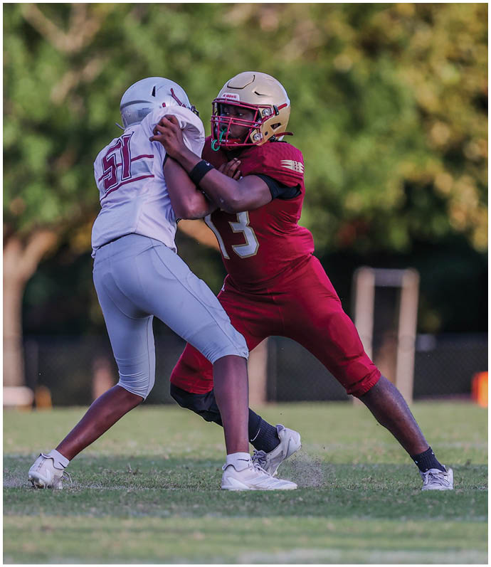Two people wearing sports uniforms are engaged in a physical struggle on a grassy field, with one in red and the other in light gray. Description generated by AI
