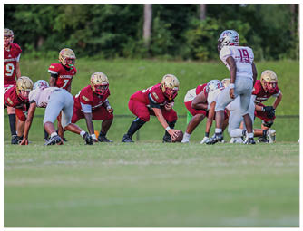 A group of people in football uniforms are lined up on a grassy field preparing for a play during a game. Description generated by AI