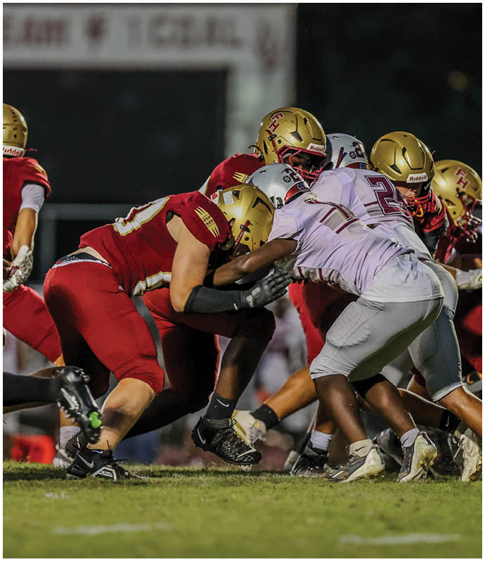 Two groups of football players in red and white uniforms are engaged in a close physical play on a grassy field during a game. Description generated by AI