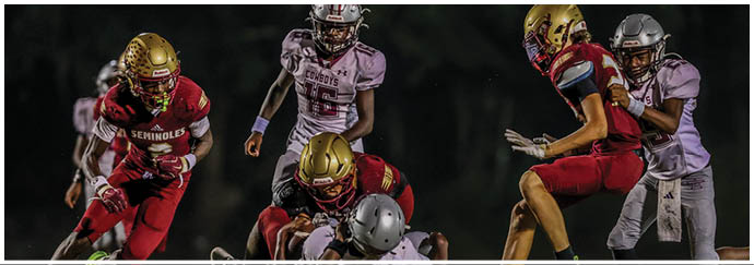 Several people wearing football helmets and uniforms are actively engaged in a nighttime football game on a field. Description generated by AI