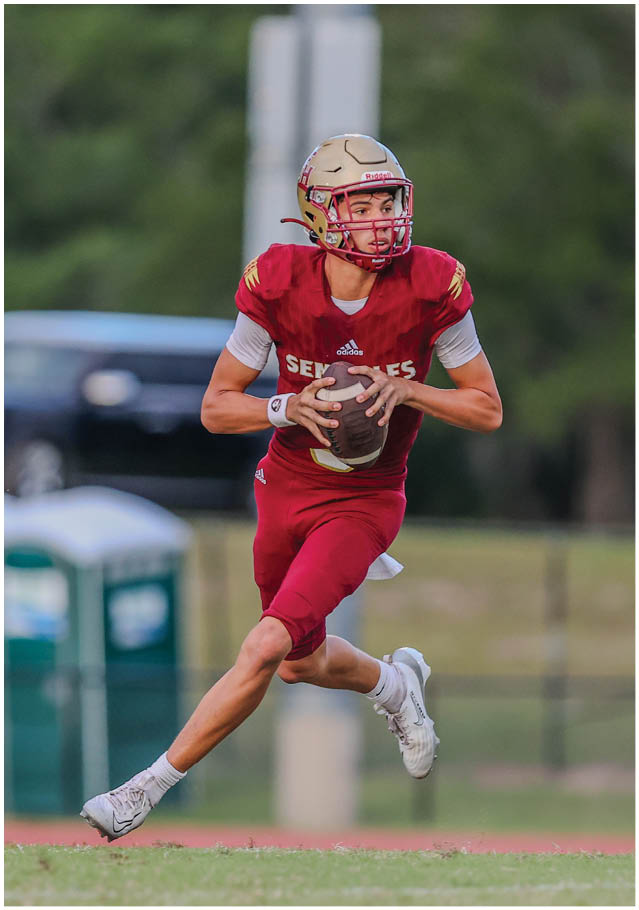 A person wearing a red football uniform and helmet is running on a field while holding a football. Description generated by AI
