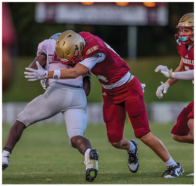 Two football players in red and white uniforms are engaged in a tackle on a grassy field while another player in red approaches from the right. Description generated by AI