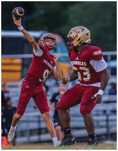 Two people in football uniforms are on a field with one person throwing a football and the other preparing to catch or block. Description generated by AI