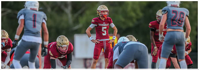People in football uniforms are lined up on a field preparing for a play during a game. Description generated by AI
