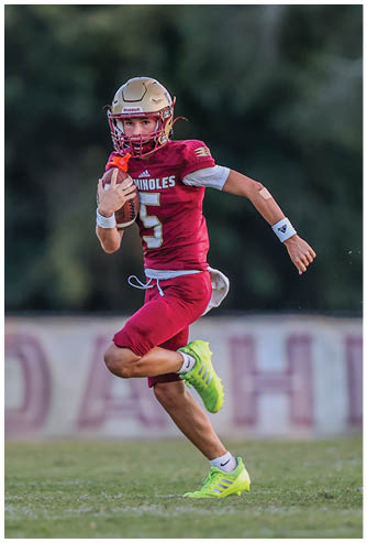 A person wearing a red football uniform and gold helmet is running on a grassy field while holding a football. Description generated by AI