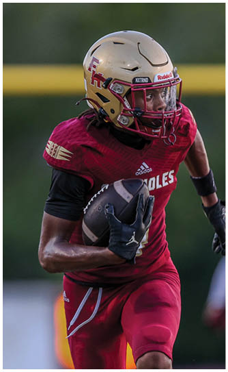 A person wearing a red football uniform and gold helmet is running while holding a football. Description generated by AI