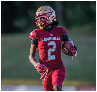 A person wearing a red Seminoles football uniform with the number 2 is running on a grassy field while holding a football, with another player in a similar uniform running behind. Description generated by AI