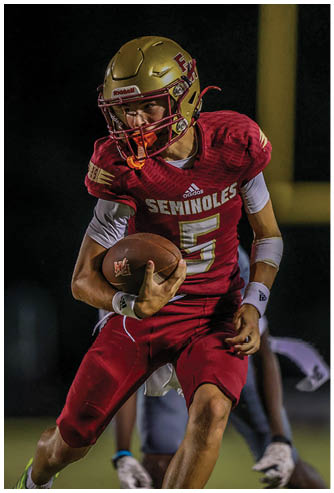 A person wearing a red football uniform with the word Seminoles and the number five is running while holding a football on a dark field. Description generated by AI