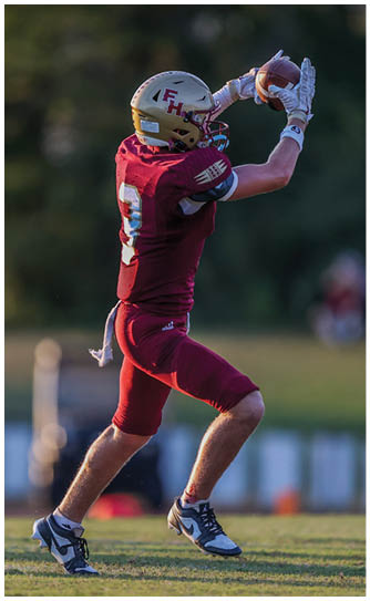 A person wearing a maroon football uniform and gold helmet is running on a grassy field. Description generated by AI