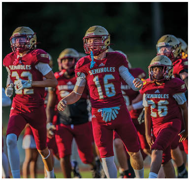 A group of people wearing maroon football uniforms with gold helmets are walking on a field during a game or practice. Description generated by AI