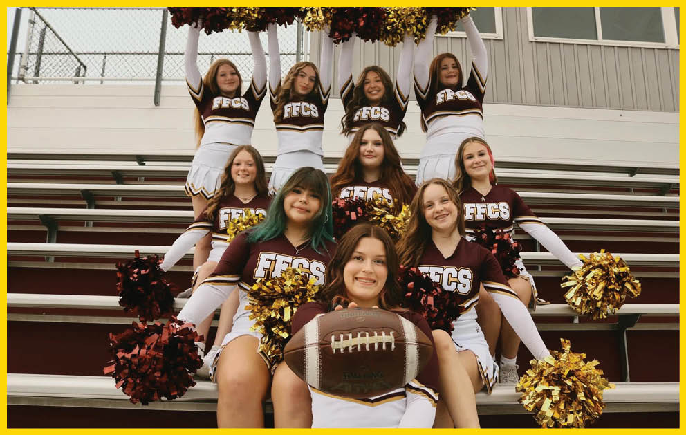 A group of cheerleaders in matching uniforms pose on bleachers with pom-poms and a football held by the person sitting in front. Description generated by AI