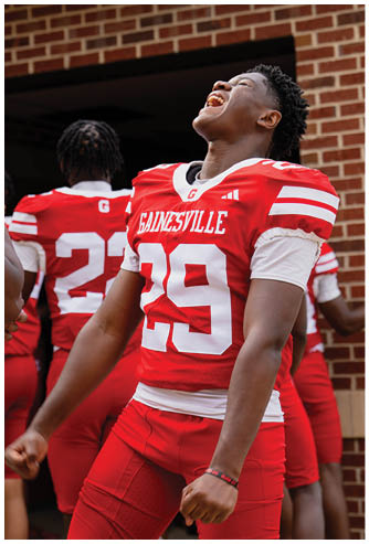 A person wearing a red and white Gainesville football jersey with the number 29 is standing with another person in a similar uniform visible in the background. Description generated by AI