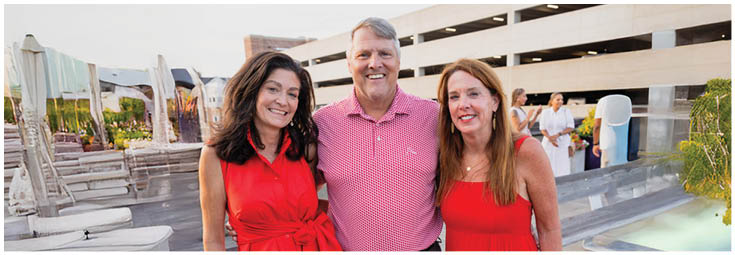 Two adults smiling and standing close together outdoors with buildings and a parking structure in the background. Description generated by AI