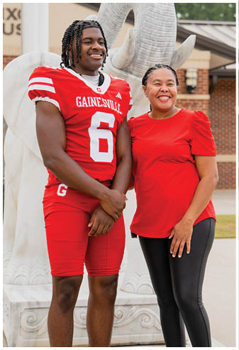 A person wearing a red Gainesville football uniform stands smiling next to another person in a red shirt and black pants in front of a large white elephant statue. Description generated by AI