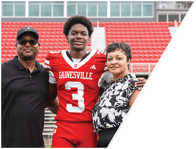 A person wearing a red Gainesville football uniform stands between two adults in casual clothing on stadium bleachers. Description generated by AI