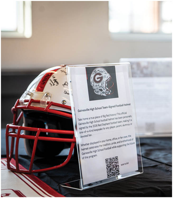 Two autographed football helmets with informational placards displayed on a table covered with a black cloth. Description generated by AI