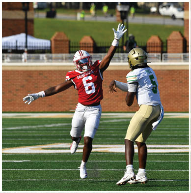 A person in a red sports uniform with the number six is jumping with one arm raised while another person in a white and gold sports uniform with the number five is preparing to throw a football on a green field. Description generated by AI