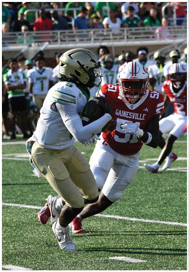 People in football uniforms are actively playing on a green field with spectators and other players visible in the background. Description generated by AI
