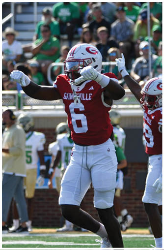 Two football players in red and white uniforms celebrate on a field with a crowd in the background. Description generated by AI