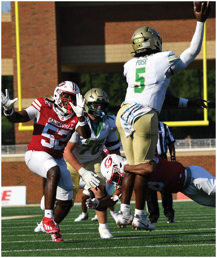 A group of football players in action on a field with one player in a red uniform reaching out while others in white and gold uniforms attempt to block or tackle. Description generated by AI