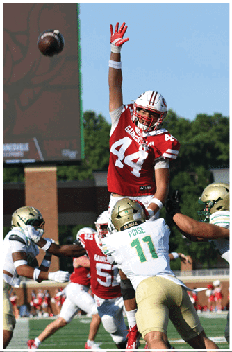 A football is captured mid-air in front of a scoreboard displaying a helmet logo and the word “WOLVES" at the top. Description generated by AI