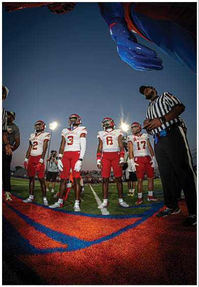 Several people wearing red helmets and sports uniforms are seen from a low angle against a clear blue sky. Description generated by AI