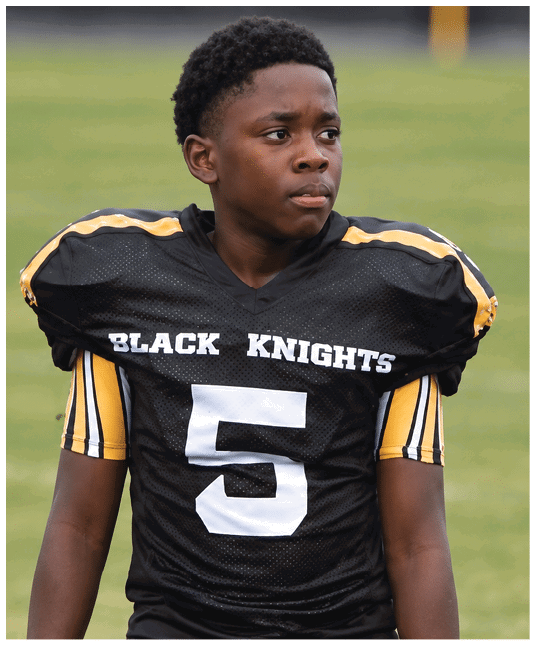 A person wearing a black sports jersey with yellow and white stripes and the words “BLACK KNIGHTS" printed on the front. Description generated by AI