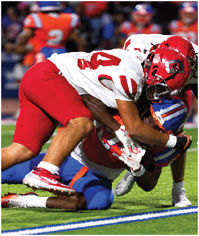 Two football players in red and white uniforms are engaged in a tackle on the field during a game. Description generated by AI