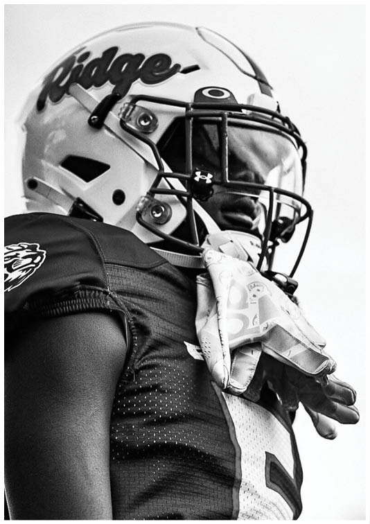 A person wearing a football helmet and jersey with the word “Ridge" on the helmet is standing and looking to the side. Description generated by AI