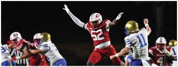 A group of people in football uniforms are actively engaged in a nighttime game with one player in a red uniform jumping with arms raised. Description generated by AI
