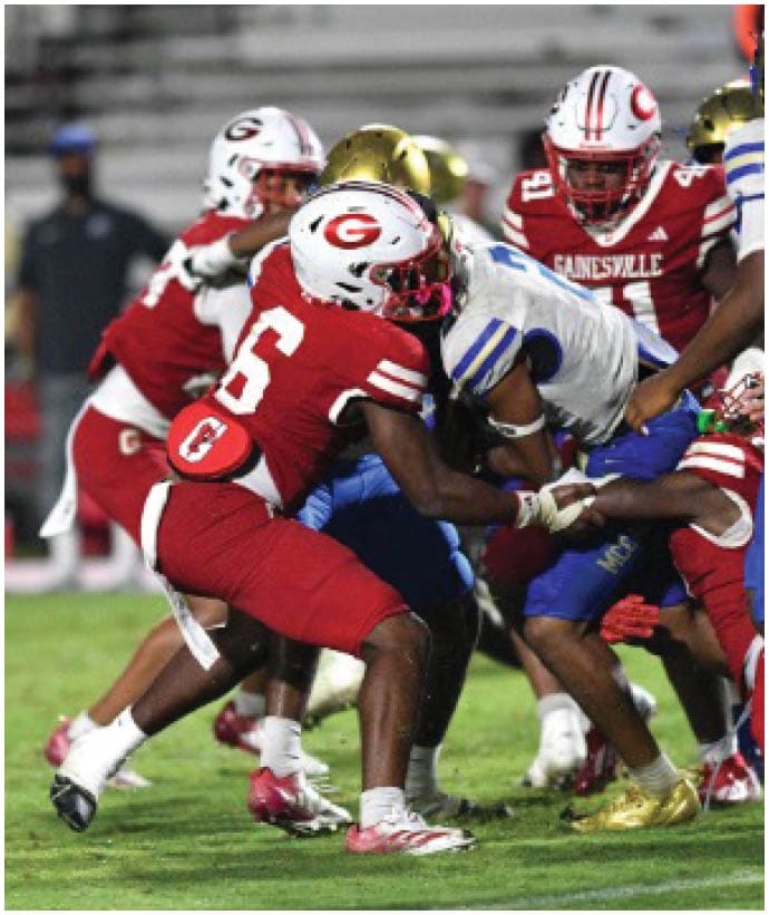 Several people in football uniforms are engaged in a tackle during a game on a grassy field. Description generated by AI