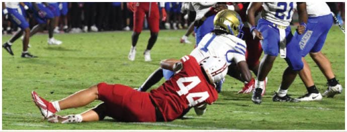 A person wearing a red sports uniform is lying on the grass field with one leg bent and the other extended. Description generated by AI