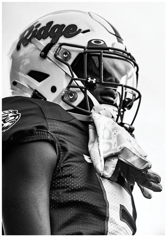 A person wearing a football helmet and jersey with the word “Ridge" on the helmet is standing and looking to the side. Description generated by AI