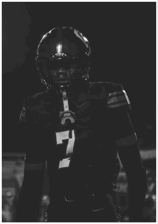 A person wearing a football uniform with the number seven stands under bright stadium lights at night. Description generated by AI