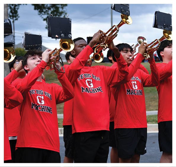 People wearing matching red shirts with “The Big Red Machine" printed on them are playing trumpets outdoors. Description generated by AI