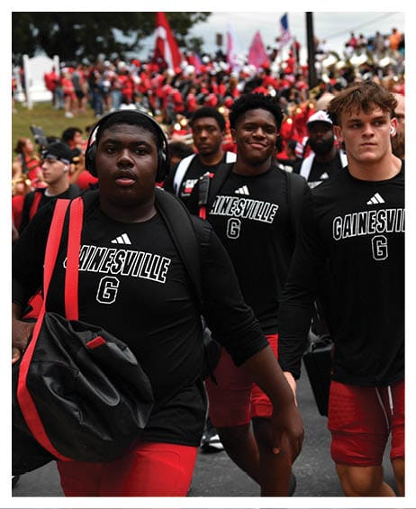 People wearing black Gainesville shirts and red shorts are walking, with one carrying a black and red bag. Description generated by AI