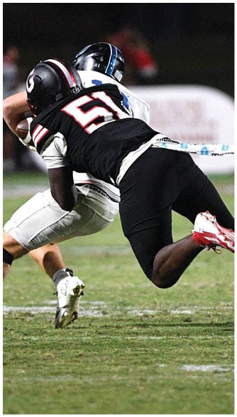 A person wearing a black and white sports uniform with cleats is diving or lunging forward on a grassy field during a nighttime sports game. Description generated by AI