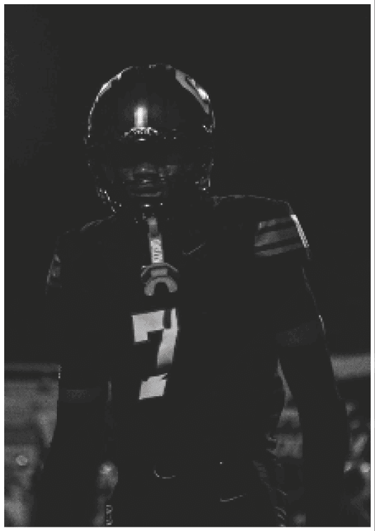 A person wearing a football uniform with the number seven stands under bright stadium lights at night. Description generated by AI