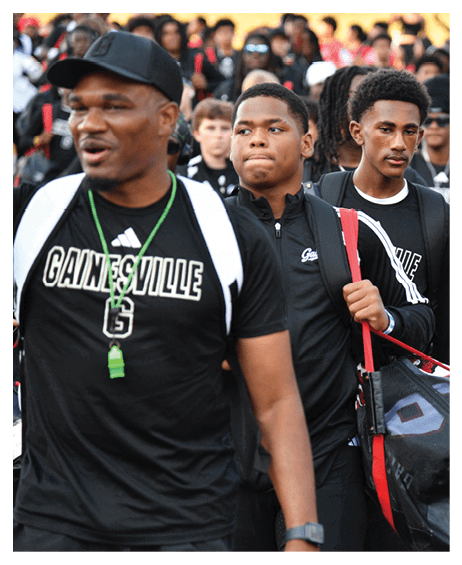 A group of people wearing sports attire and backpacks walk closely together, with one person carrying a large sports bag. Description generated by AI