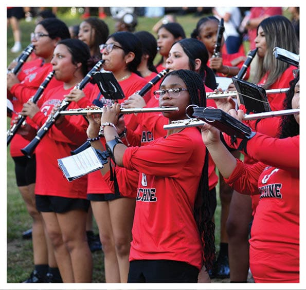 A group of people wearing matching red shirts are playing flutes and clarinets outdoors in a coordinated band formation. Description generated by AI